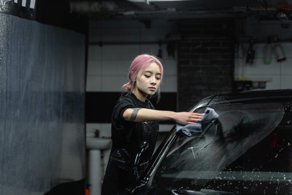 Asian woman with dyed hair cleaning a car windshield indoors. Artistic and detailed composition.