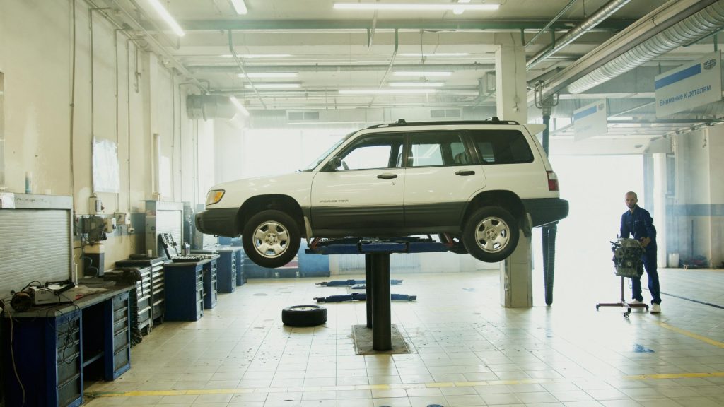 Mechanic repairing a car on a lift in a well-equipped garage.